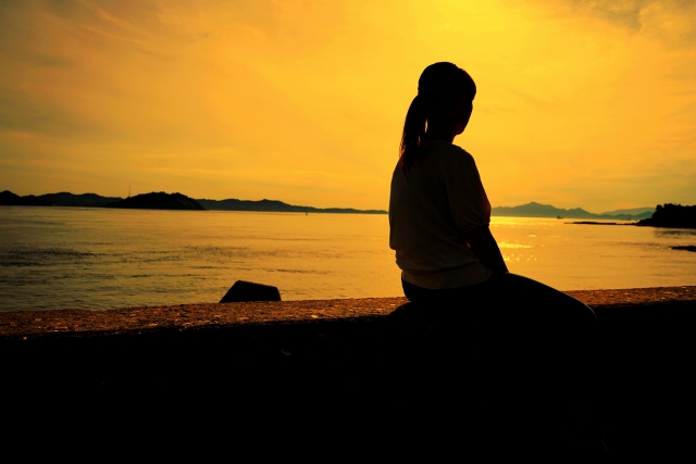 夕日の中で防波堤に座る女性